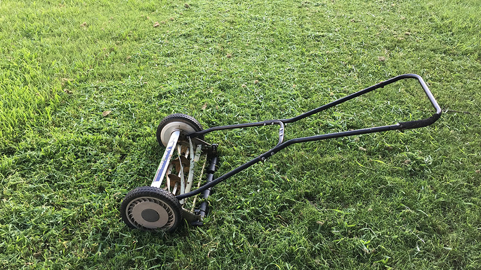 En handgräsklippare står på en nyklippt gräsmatta.
