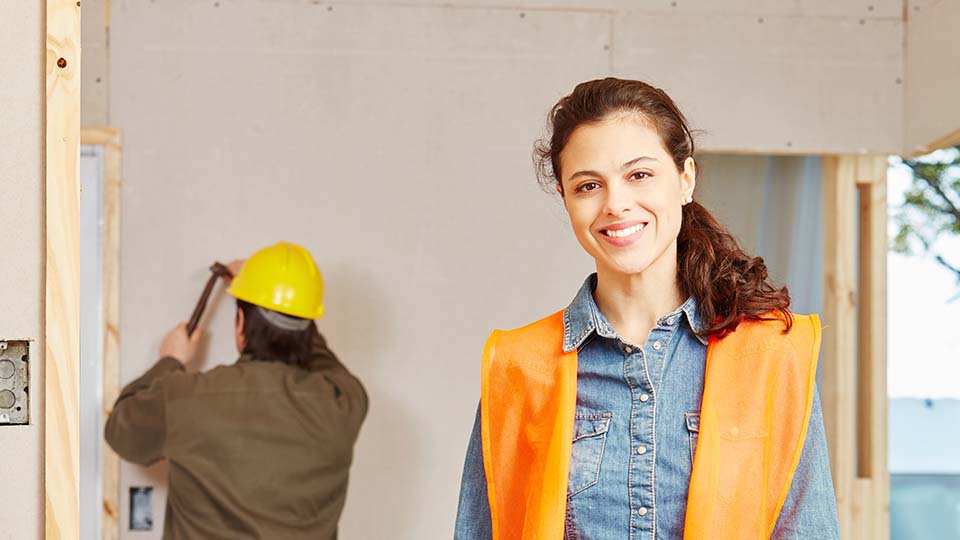 Ung kvinna i arbetskläder på byggarbetsplats